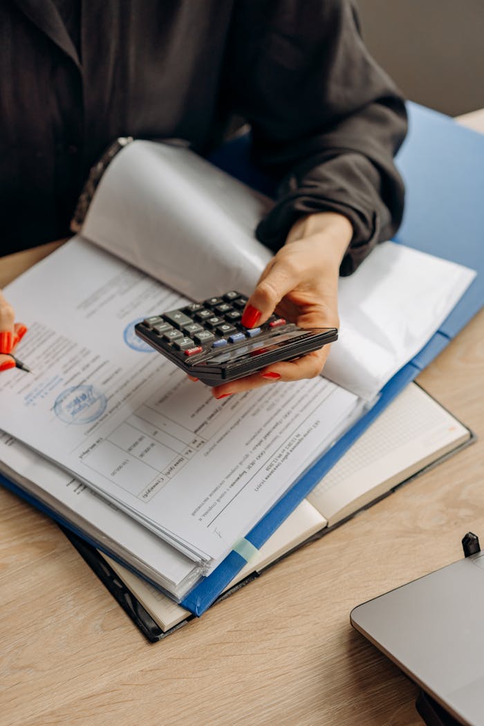 why-choose-us-02 Person using calculator and documents for accounting tasks in an office setting.