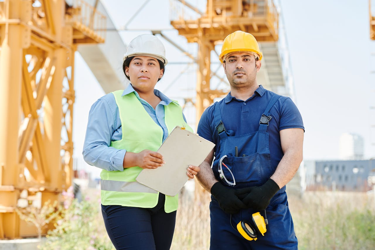 about-01 Two engineers at a construction site wearing hard hats and safety vests, standing confidently.