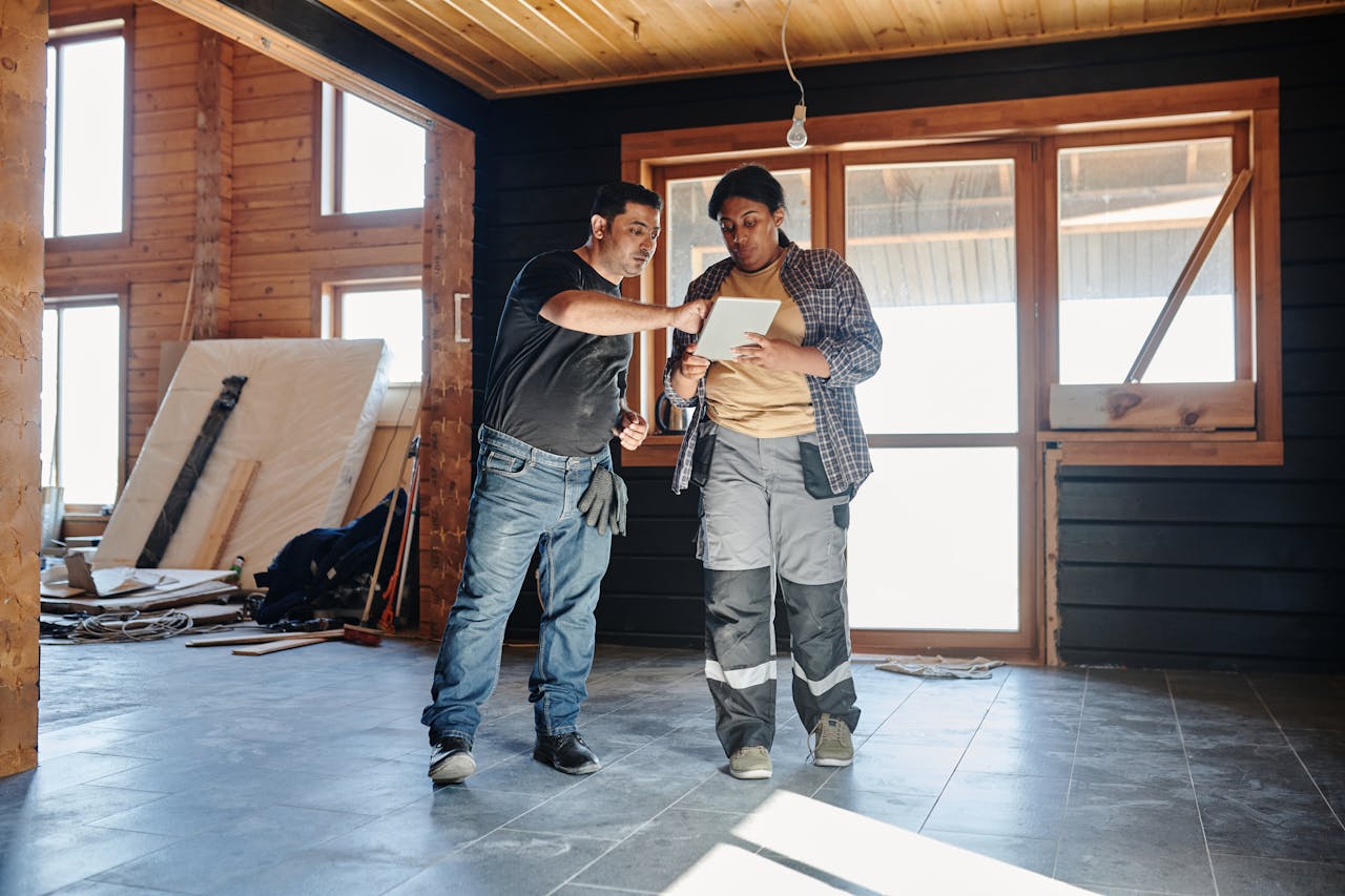 services-02 Two construction workers inside a house reviewing renovation plans on a digital tablet.